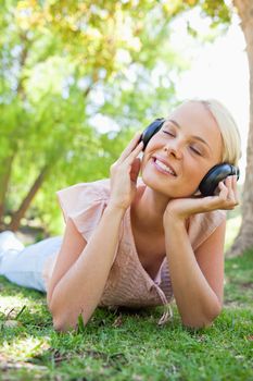 Smiling young woman with headphones enjoying music on the lawn