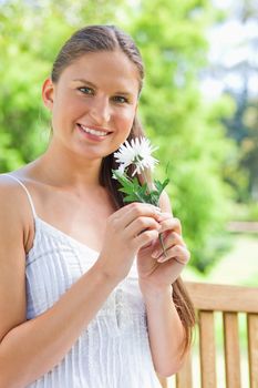 Smiling young woman with a flower sitting on a bench