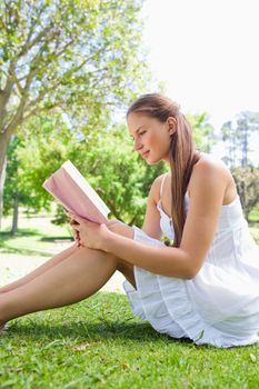 Side view of a smiling woman reading a book on the grass