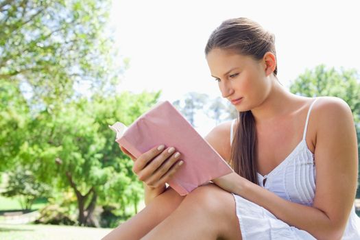 Side view of a young woman reading a novel in the park