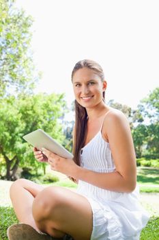 Side view of a smiling young woman sitting on the lawn with a tablet computer