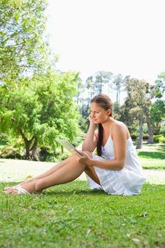 Side view of a young woman with her tablet computer sitting on the lawn