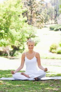 Smiling young woman sitting in a yoga position in the park