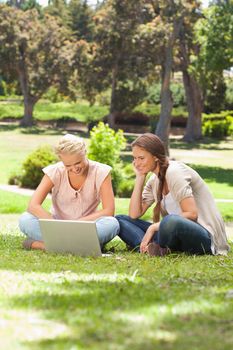Smiling female friends with a laptop sitting on the lawn