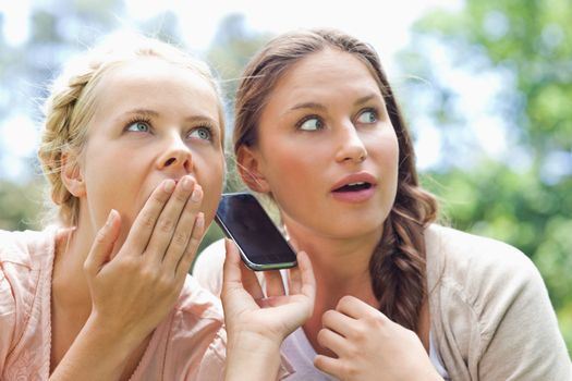 Female friends listening to a phone call in the park