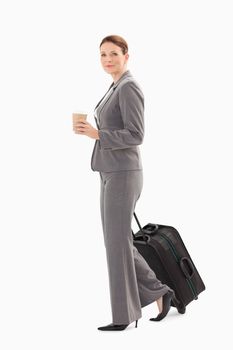 A businesswoman is walking with coffee and suitcase