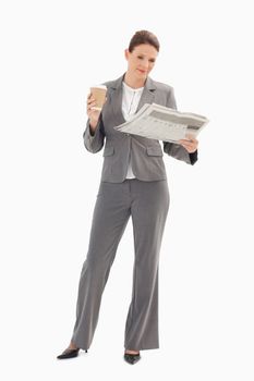 A businesswoman is reading the newspaper and holding a cup of coffee