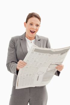 A surprised businesswoman is standing reading the newspaper