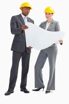 A businessman and woman with hard hats on holding a paper sheet