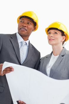Two business people are wearing hard hats and holding a paper