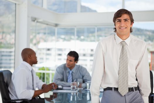 A smiling young businessman is leaning on a table