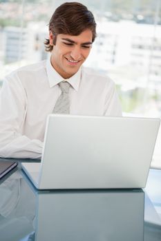 A smiling young businessman is on his laptop