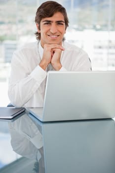 A smiling young businessman is resting his head on his hands