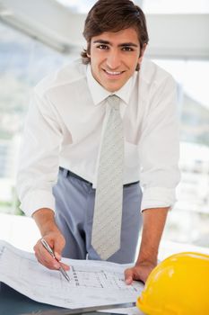 A smiling businessman with some blueprints and a hard hat on a table