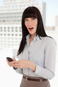 A woman at work with her mobile in hand looking up and shocked after reading her text message