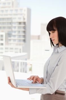 A woman with a laptop in her hand uses it while at work