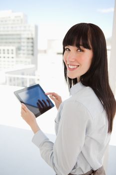 A smiling woman looking into the camera as she has a tablet pc in her hands