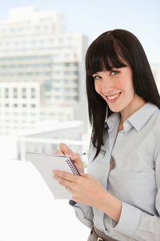 A business woman in her office looking at the camera as she writes on a notepad 