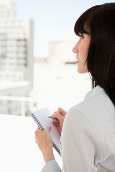 A business woman looks upwards as she stops writing on the notepad in her hand