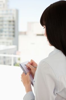 A business woman with her back to the camera begins to write down information that she has though of