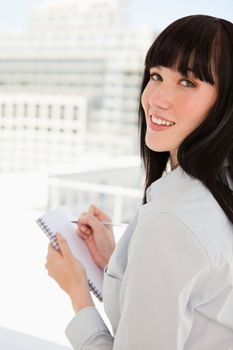 A smiling woman looking at the camera with a notepad in her hand