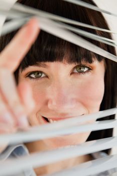 A close up shot of a woman looking through blinds straight ahead