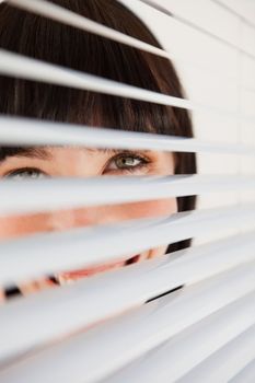 A woman smiling as she glances into the camera through some blinds
