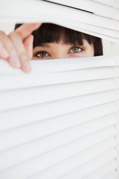 A woman looking through a set of closed blinds by opening a part with her fingers