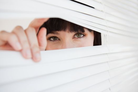 A woman looking through a closed set of blinds by opening them with her fingers