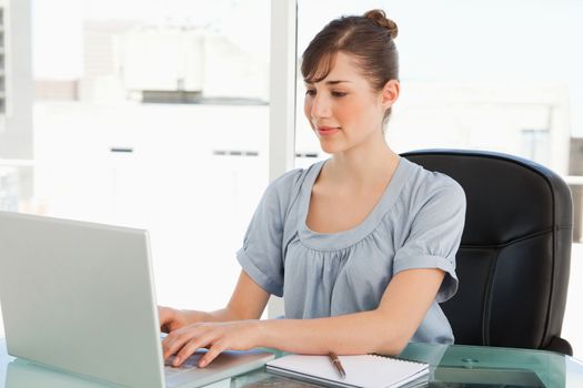 A smiling employee sits at her office and types on her laptop