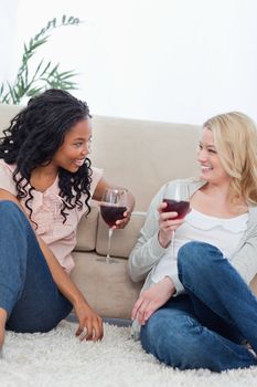 Two women are sitting on the ground and leaning against a couch