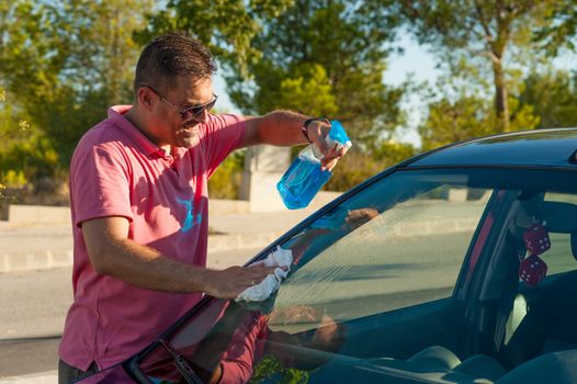 Male cleaning his car windscreen outdoors