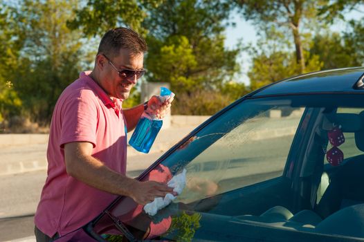 Hispanic male cleaning his car windscreen