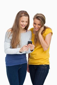 Two females student smiling while looking a cellphone against white background