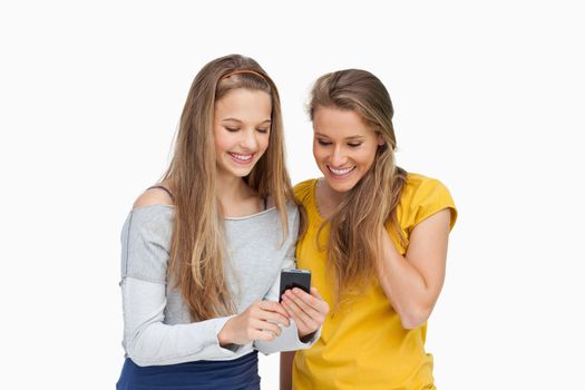 Two smiling students looking a cellphone screen against white background
