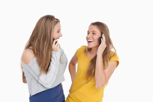Two young women laughing on the phone together against white background