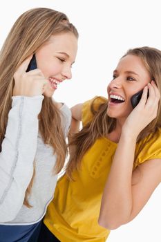 Close-up of two beautiful students laughing on the phone against white background