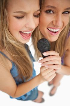 High-angle shot of two happy young blonde singing against white background