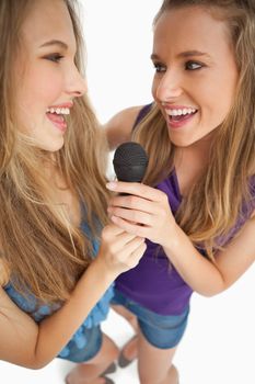 High-angle shot of two happy young beauty singing together against white background