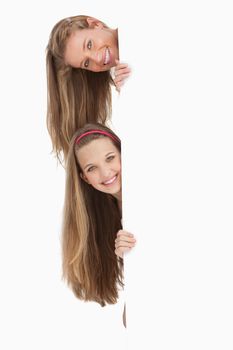 Close-up of two long hair students behind a blank sign against white background