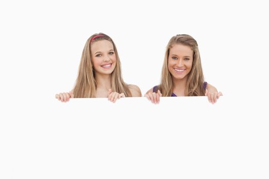 Close-up of two young women holding a blank sign against white background