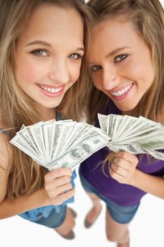High-angle shot of two happy young beauty holding dollars against white background
