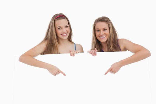 Portrait of young women holding and pointing a blank sign against white background