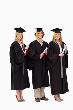 Three smiling students in graduate robe holding a diploma against white background