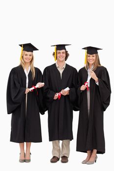 Three students in graduate robe holding a diploma against white background