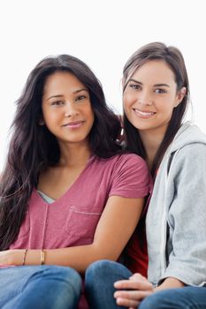 A half length shot of two women on the couch looking towards the camera while they both smile