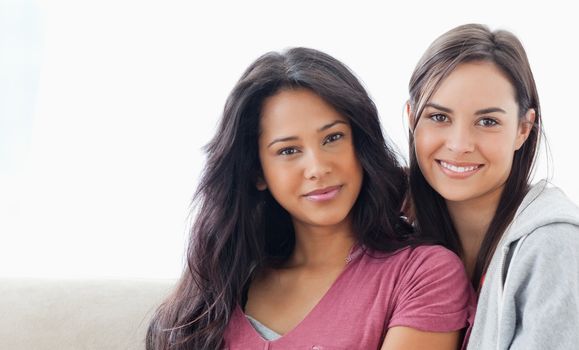 A head and shoulder shot of two women lying against one another and smiling as they both look into the camera