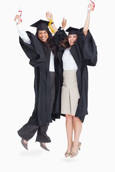 A full length shot of two women jumping in celebration after graduating 