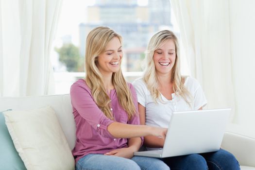 Two women laughing together as they look at something on the laptop in their hands 