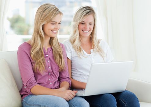 A smiling woman and her friend sitting together as they use a laptop 